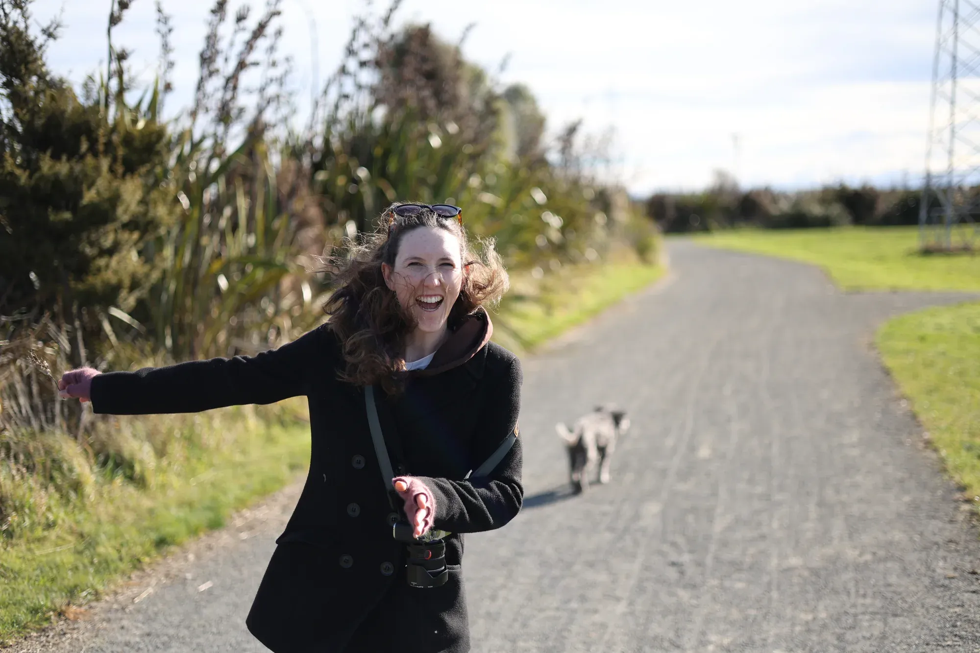 Caitlin laughs on a sunny camera walk with Jasper following behind her