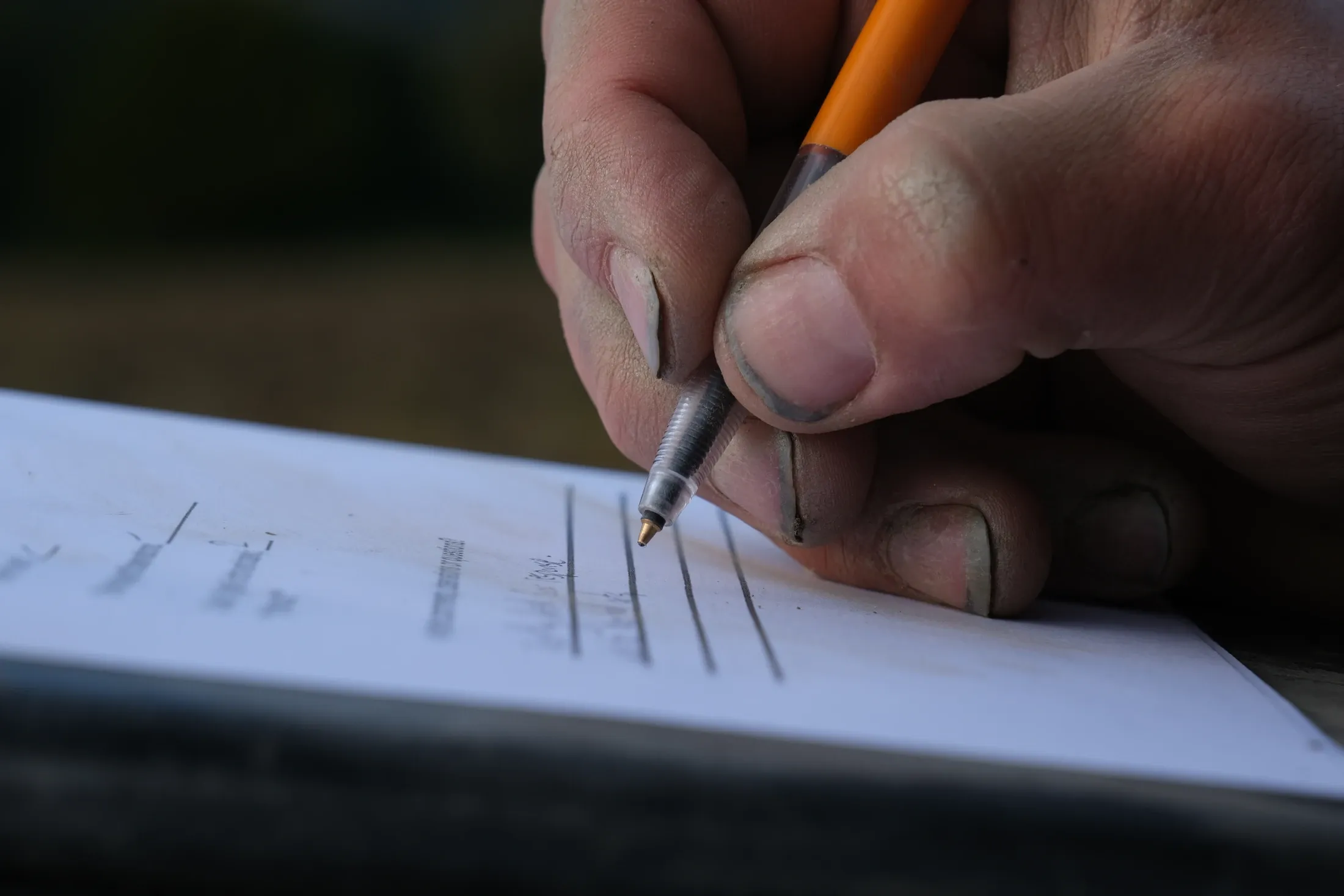 Soil-covered hands hold a pencil while making notes on a form