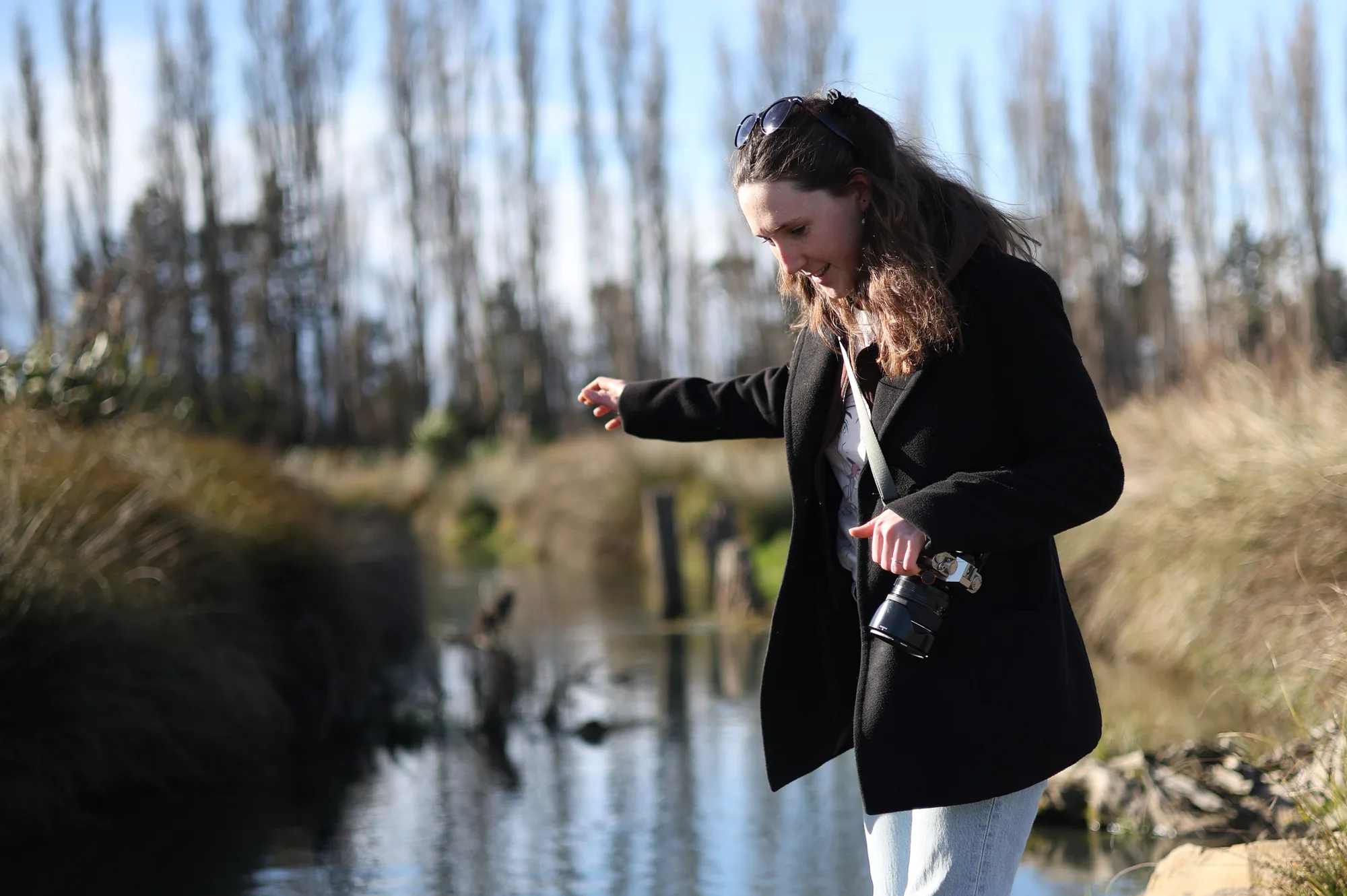 Caitlin walks beside a stream with her Fujifilm camera in hand